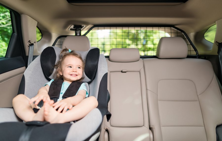 Ein kleines Mädchen sitzt in ihrem Kindersitz auf der Rückbank eines Autos. Es lacht und schaut aus dem Fenster.