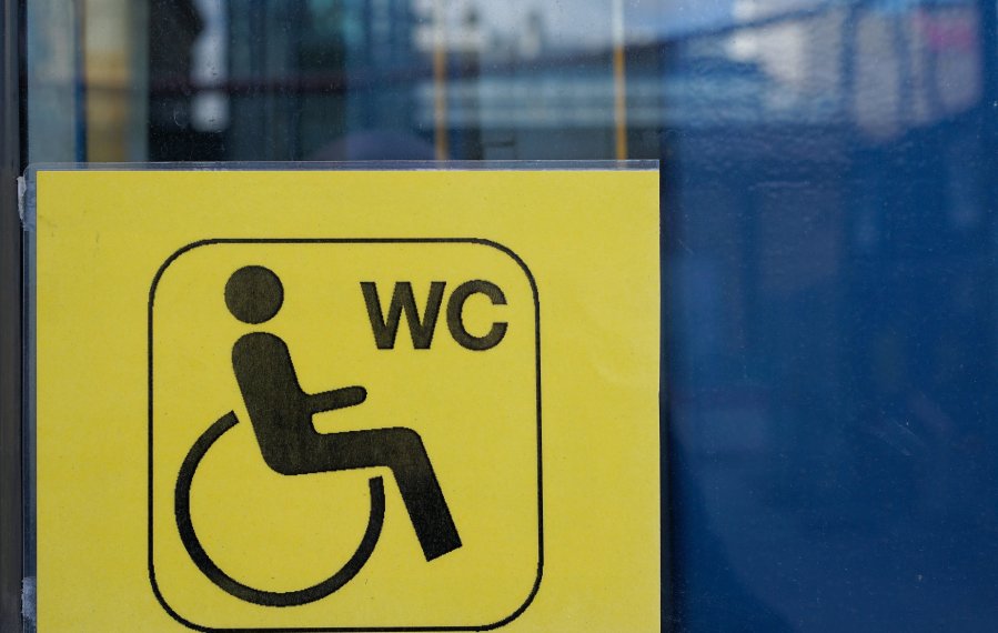 Ein schwarz bedrucktes Symbolbild mit einem Rollstuhlfahrer und dem WC-Zeichen auf einer gelben, einlaminierten Karte.