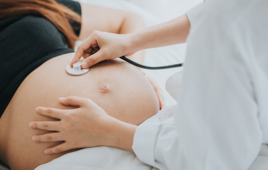 Eine schwangere Frau ist beim Arzt. Dieser hört den Bauch mit dem Stethoskop ab.