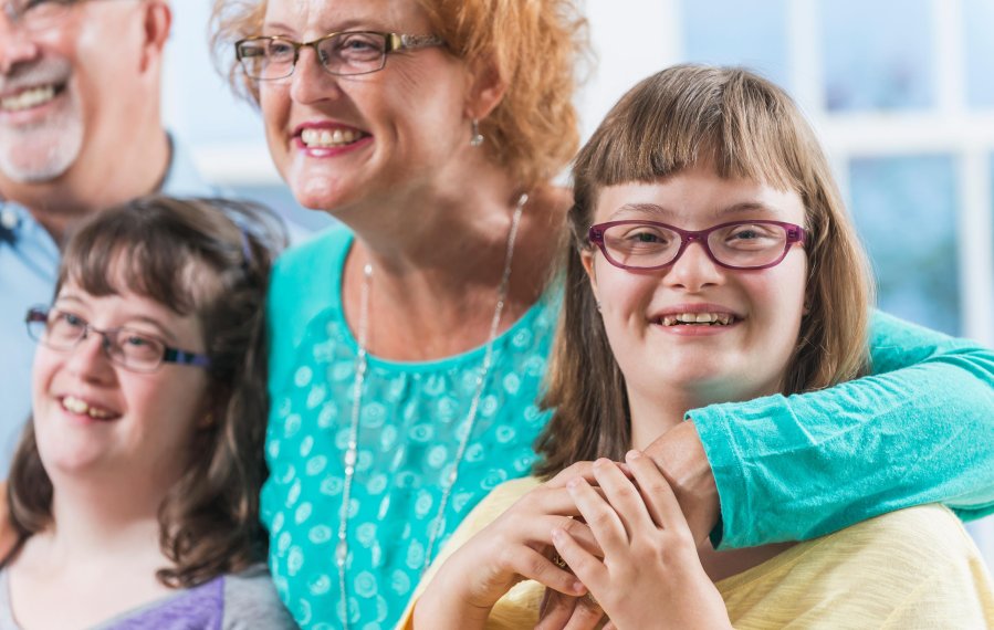 Ein Familienfoto mit den Eltern und zwei Töchtern mit Down-Syndrom. Alle lachen.