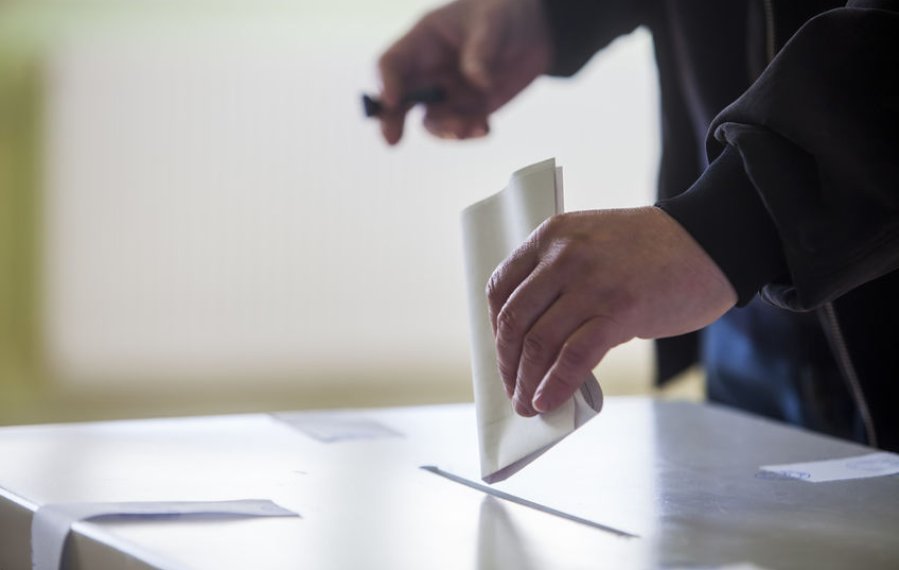 Nahaufnahme: Eine Person wirft einen Wahlzettel in eine Wahlurne.