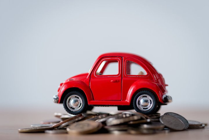 Fahrkosten - ein kleines rotes Spielzeugauto steht auf einem Berg mit Geldmünzen. Die Münzen liegen auf einem Tisch.