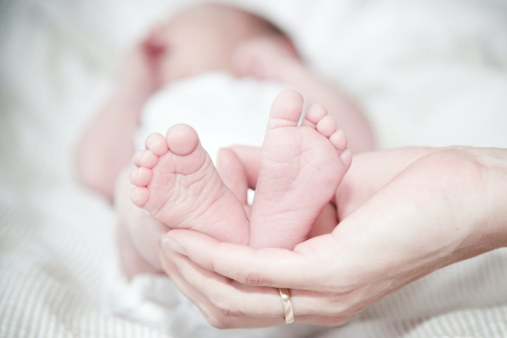 Behinderungen durch Geburtskomplikationen (perinatal) - Nahaufnahme: Eine Hand hält die Füße eines liegenden Babys.