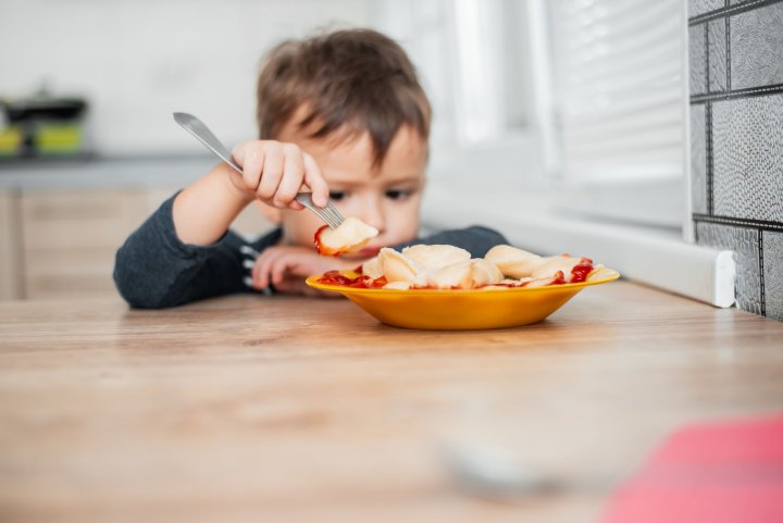 Diagnose Prader-Willi-Syndrom - Ein kleiner Junge sitzt vor seinem Teller mit Nudeln. Er hat die Gabel in der Hand und stützt sein Kinn auf dem anderen Unterarm ab. Er sieht nachdenklich aus.