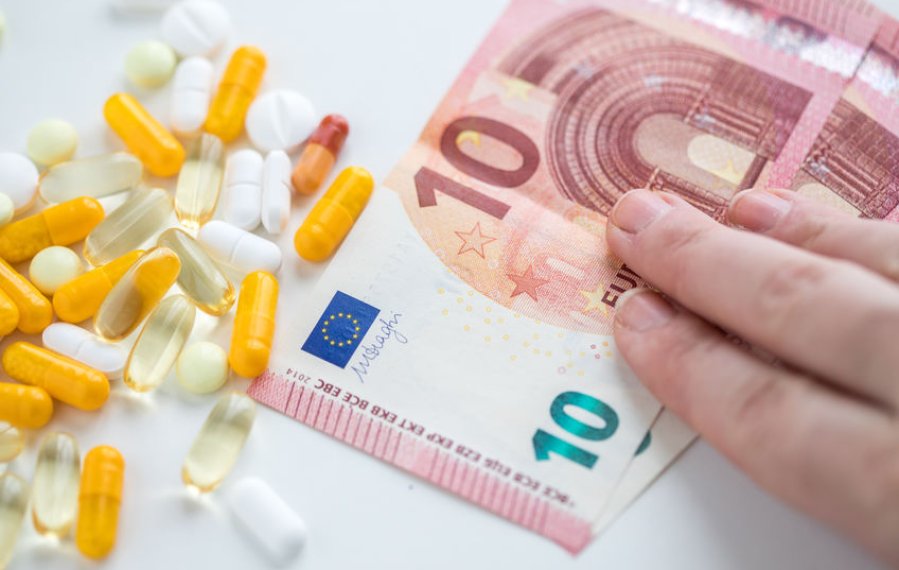 Zuzahlung -  auf einem Tisch liegen zwei 10 Euroscheine, auf denen eine Hand liegt, und verschiedene Tabletten.