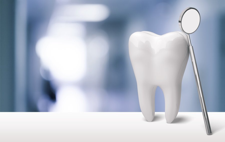 Ein weißer Zahn steht auf einem weißen Untergrund. An dem Zahn angelehnt ist ein kleiner Mundspiegel. Der Hintergrund ist unscharf.