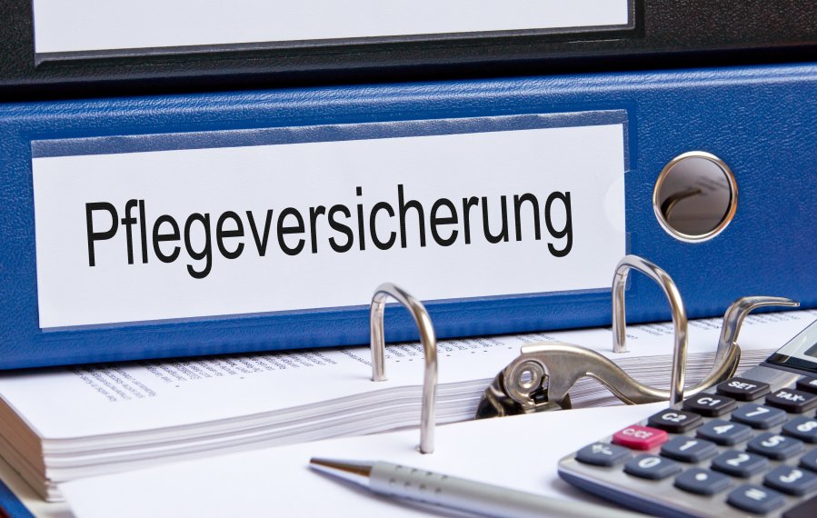 Drei Ordner. Ein Ordner ist aufgeschlagen und auf ihm liegt ein Taschenrechner. Im Hintergrund steht auf dem Rücken eines Ordners "Pflegeversicherung".