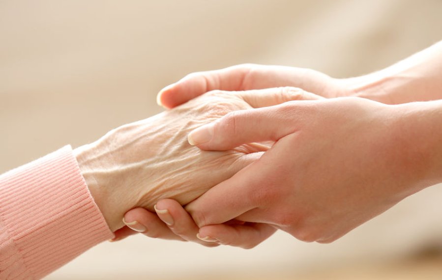 Nahaufnahme: Zwei Hände einer Person umschließen sanft eine Hand einer älteren Person.