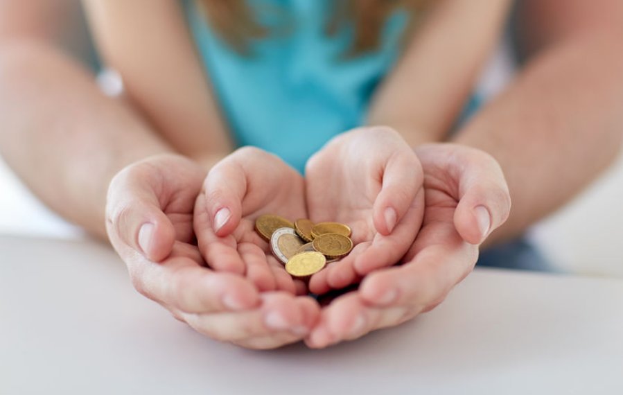 Nachteilsausgleiche und Ermäßigungen - In den Händen einer erwachsenen Person liegen die Hände eines Kindes. In den Händen des Kindes liegen Euromünzen. 