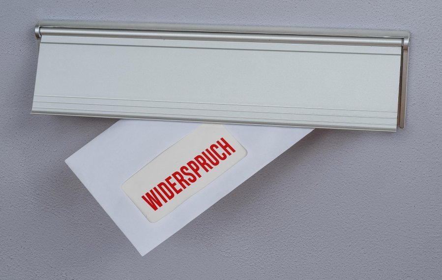 Ein Briefumschlag schaut aus einem Briefkasten heraus. Auf dem Briefumschlag steht „Widerspruch“ geschrieben.