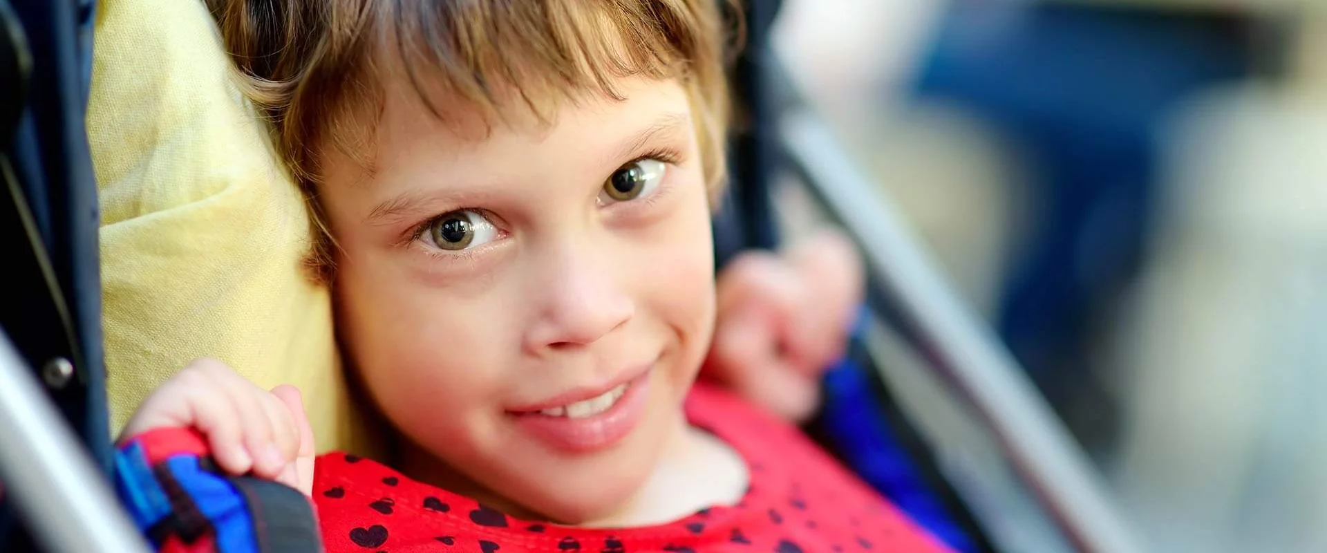 Ein Mädchen sitzt im Kinderwagen. Sie schaut in die Kamera und lächelt.